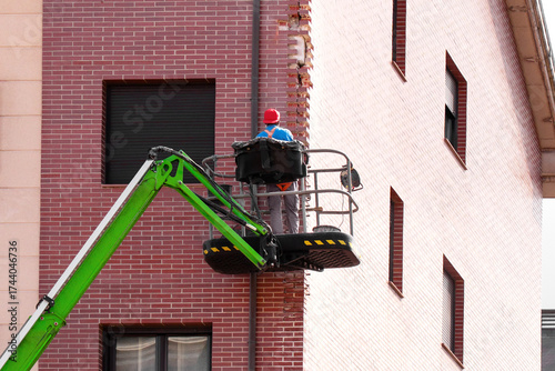 Construction worker in uniform and red cap repairing exterior brick corner wall of residential building in aerial lift basket