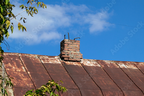 Brick chimney of an old abandoned house with a rusty iron roof