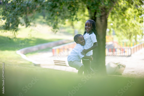 Playful brother hugging sister outdoors in park during carefree joyful summer sunny afternoon