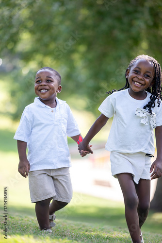 Joyful young siblings smiling widely holding hands outdoors during carefree playful summer sunny afternoon