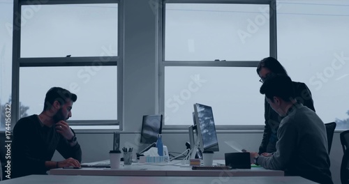 Collaborating professionals reviewing monitors and typing on laptop in office, with coffee cup