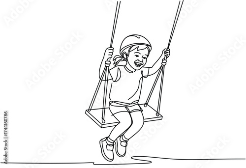 Joyful young child wearing a helmet laughs while swinging high on a playground swing set