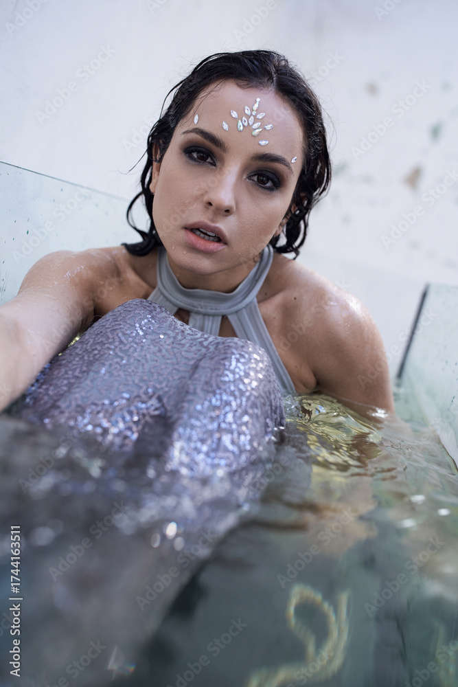 Obraz premium Young woman in shimmering attire poses gracefully in serene water setting