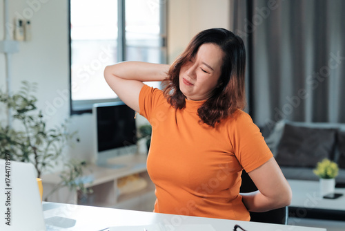 Foto Asian woman feeling pain in her back and neck while working from home, experienc