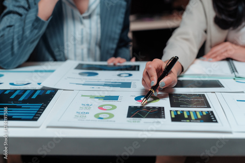 Foto Businesswomen examining financial data, using a pen to point at charts and graph