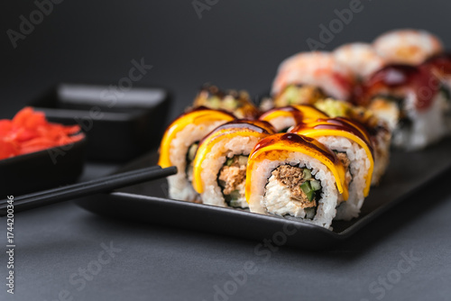 Sushi roll with salmon,  avocado and tuna. Sushi set served on the black plate next to red ginger with black sticks on the black background