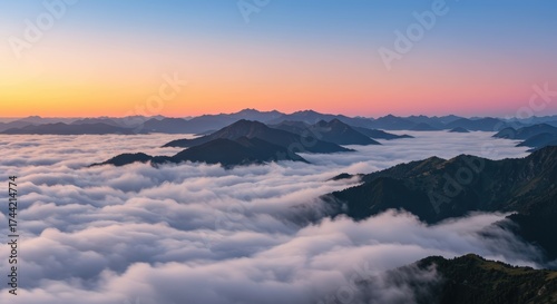 Stunning panoramic view of mountain peaks emerging from a sea of fluffy white clouds, showcasing the beauty of a colorful sunset sky filled with orange, pink, and blue hues reflecting serene natural.