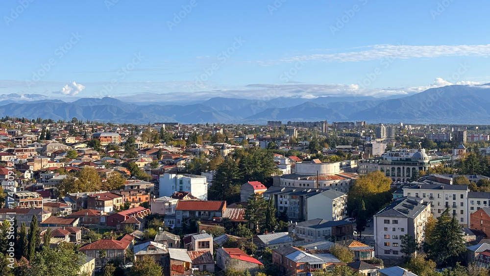Obraz premium Kutaisi, Georgia: Panoramic urban view. Red-roofed houses, modern buildings, and distant mountains under a clear sky. A vibrant, historic city.