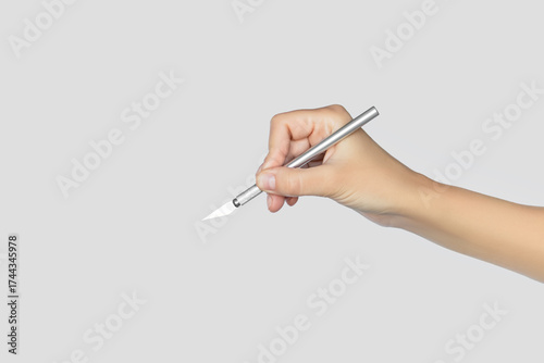 Hand holding an Exacto knife against a neutral background