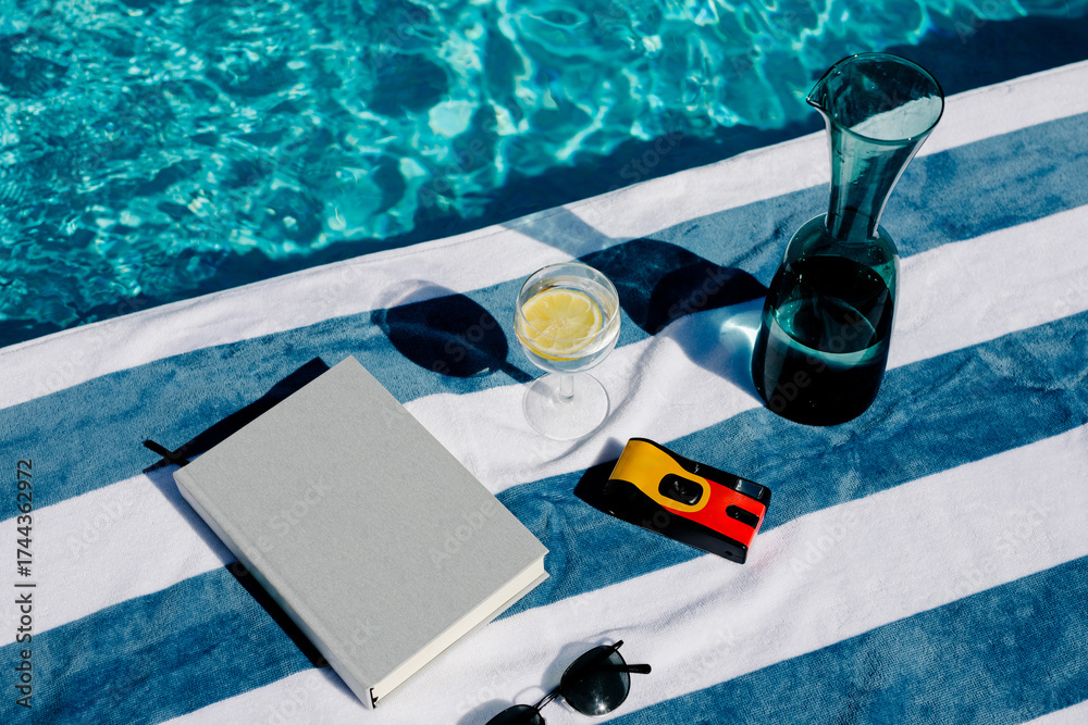 Still life showing summer objects next to a pool on a striped towel