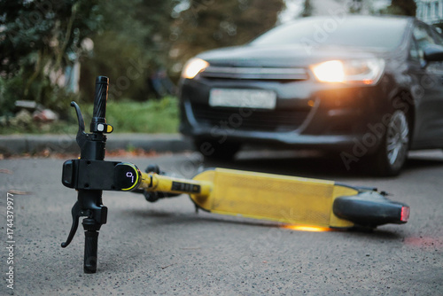 Yellow electric scooter lying on road near car closeup. Traffic accidents with scooter.