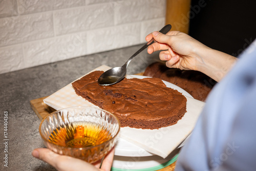 Woman hands adding sirup into a chocolate cake. Cooking for dinner party.