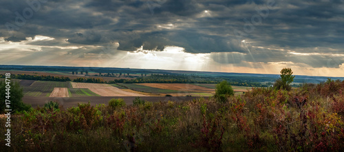 a dark sky with dramatic sun rays at Autumn landscape with fields on the horizon