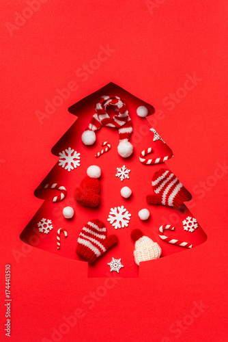 Red Christmas tree cutout with knitted mittens, hats, and candy canes inside. Cozy winter holiday concept.