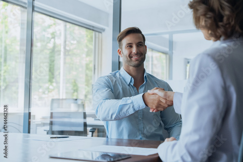 Young Latin bank worker man shaking hand with client, recruit employee on interview or business partner after signing contract. Group of people satisfied with results of team work together. Copy space