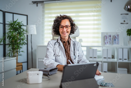 Photos mature woman doctor sit at the table and use digital tablet at office
