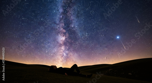 Woman lying down on a hill looking up at the milky way and shooting stars, concept of dreaming and stargazing.