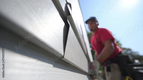 A worker installing plastic a panel siding on the outside wall of the residential house