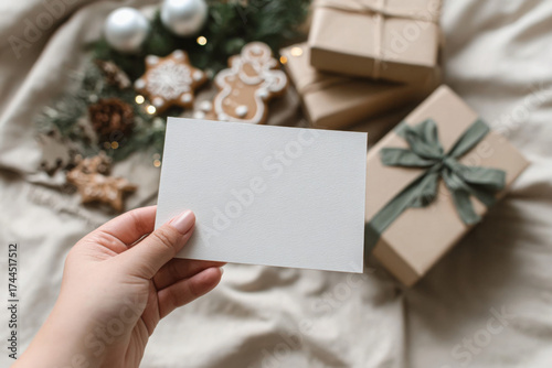 Blank greeting card held in hand surrounded by Christmas gifts and decorations perfect for holiday wishes and personalized messages
