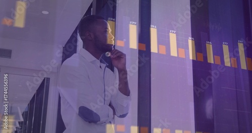 Obraz na plátně Man wearing shirt analyzing bar charts in corporate hallway, with tinted glass w