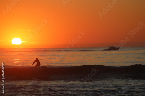 silhouette of a surfer and boat with sunrise background