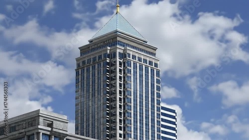 Tall building with a bluestriped pyramid roof against a blue sky with clouds