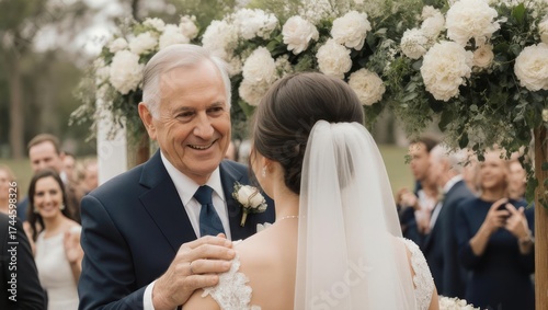 Father smiles at daughter at wedding ceremony, decorated floral arch, guests in background