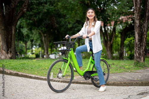 Quadro em tela Pretty asian woman smiling while stopping a green bicycle by the road in nature park