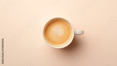 Overhead view of a white coffee mug filled with light brown coffee on a pale peach background