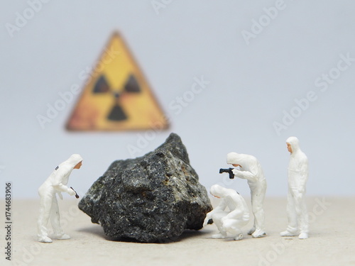 Mini toy of action figure at table with blur background. Miniature photography concept design. Minifigure of worker character wearing hazmat suit with uranium stone and radioactive symbol.