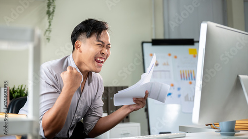 Fotografija Excited asian businessman office worker looking at computer raised hands holding