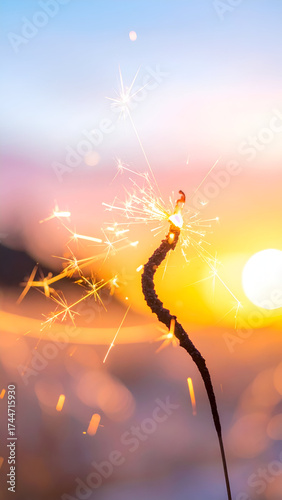 Sparkler burning brightly against a vibrant sunset sky with warm colors and soft clouds.