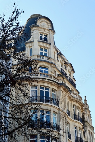 Ornate corner building facade featuring architectural details, mascarons, balconies, and mansard roof against a blue sky. Antwerp, Belgium