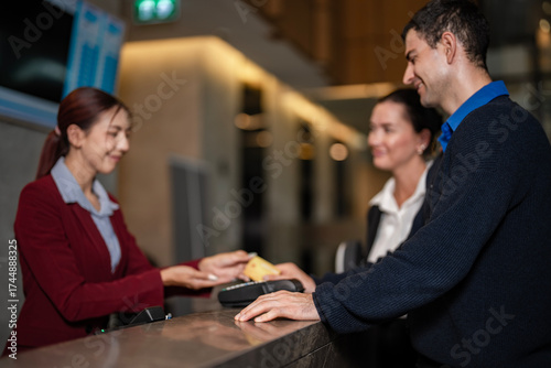 Hotel employee completing guest transaction at front desk with credit card machine. Perfect for travel, hospitality, and booking services. Digital cashless society and lifestyle concept.