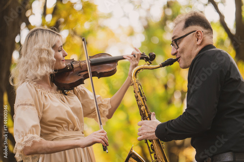 Beautiful blonde violinist and saxophonist perform melodies in autumn park. Fantastic romantic mood, a touch of autumn. Musical instruments  playing at an outdoor concert. A musical duet. Portrait