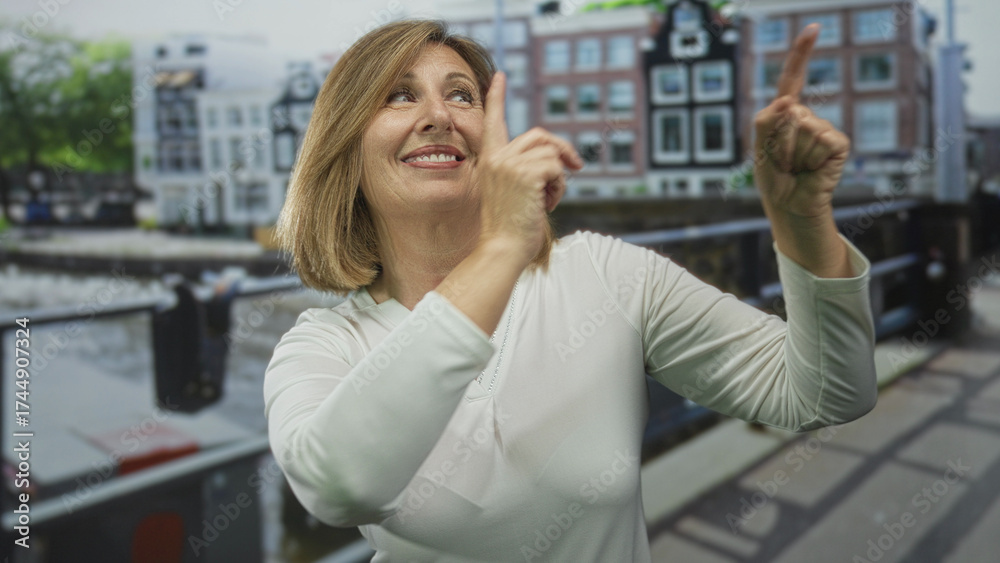 Fototapeta premium Middle-aged woman wearing white top points finger at metal canal railing on city street; joy celebration.