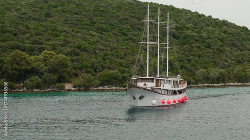 A traditional wooden gulet, a charter boat for tourist excursions, cruises in a calm bay on a cloudy day. This peaceful scene shows a scenic journey along the green Adriatic coast of Croatia.