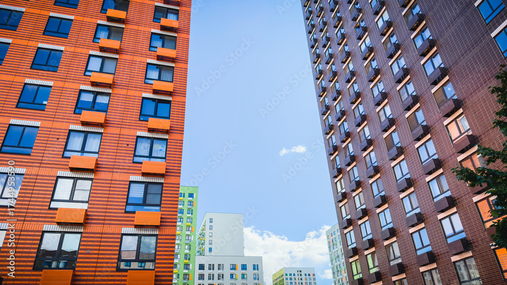 Fototapeta premium Colorful modern high-rise residential buildings with geometric facades and balconies against blue sky, representing contemporary urban architecture, housing development, and real estate investment