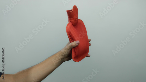 Man holding a red hot water bottle against a plain white background, showcasing the comfort item in an isolated setting.