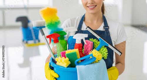 Smiling woman holding a bucket filled with various cleaning supplies, ready to clean.