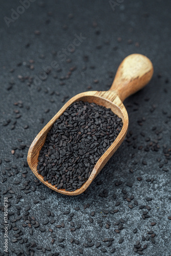 Wooden scoop filled with black sesame seeds on dark background