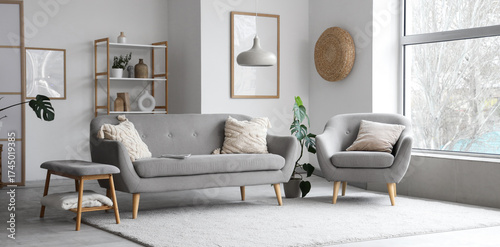 Interior of light living room with grey sofa, armchair and soft bench