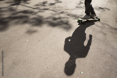 body shadow of unrecognizable skateboarder riding by sidewalk in city park