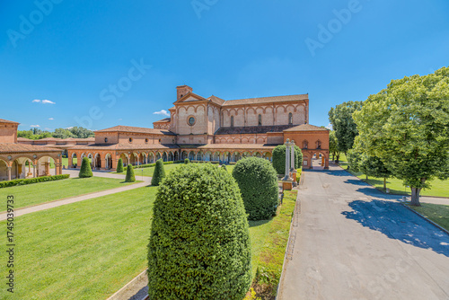 Saint Christopher Church of the Charterhouse of Ferrara, featuring a unique cotto brick facade, rises majestically under a clear blue sky amidst lush green lawns and trees in Ferrara city of Italy