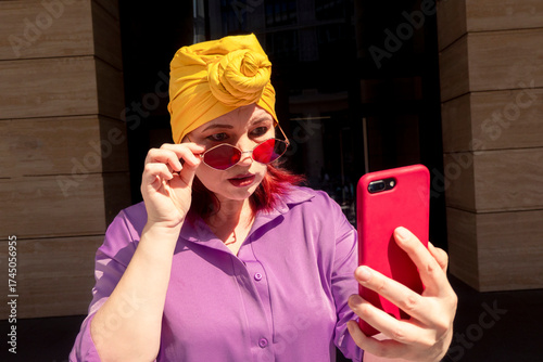 Happy and funny cool lady with fashionable clothes on dark background look to the phone with different emotions - adult asian with extravagant style, concepts about lifestyle, fasion and elderly