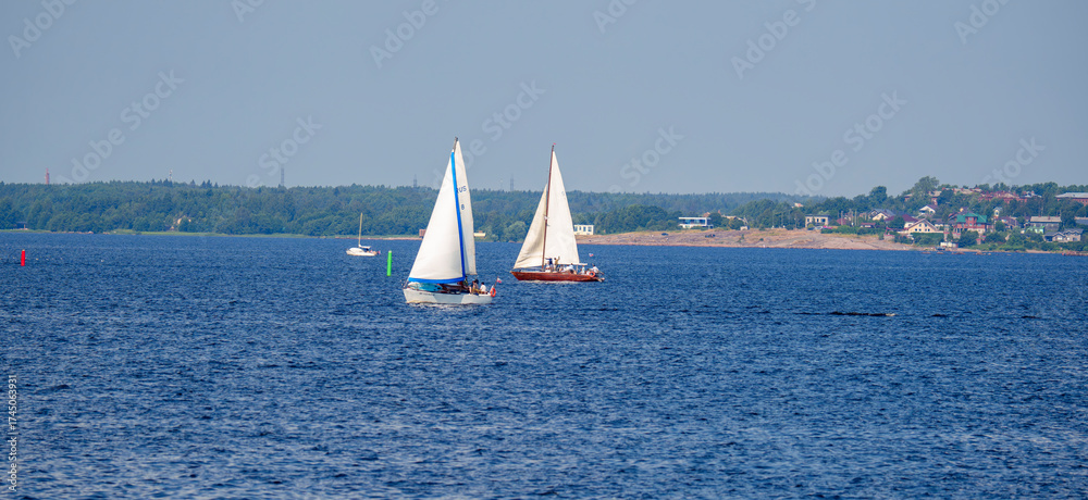 Fototapeta premium Two sailboats on lake near coastal town on a summer day