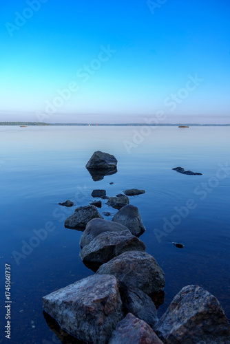 Calm lake with rocks in still water under blue sky at dawn