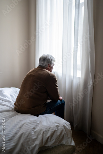 Fotografie Sad old man in emotional numbness, physical fatigue and cognitive deterioration sit on bed and look out window