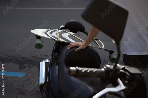 hand of man attached skateboard to back seat of motorbike outdoors