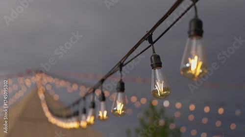 Experience the enchanting atmosphere of glowing string lights hanging beautifully against a darkening sky, enhanced by a soft, blurred background and charming bokeh effects that invite warmth.